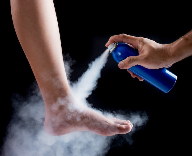 Analgesic spray can spraying on foot with black background,medical concept