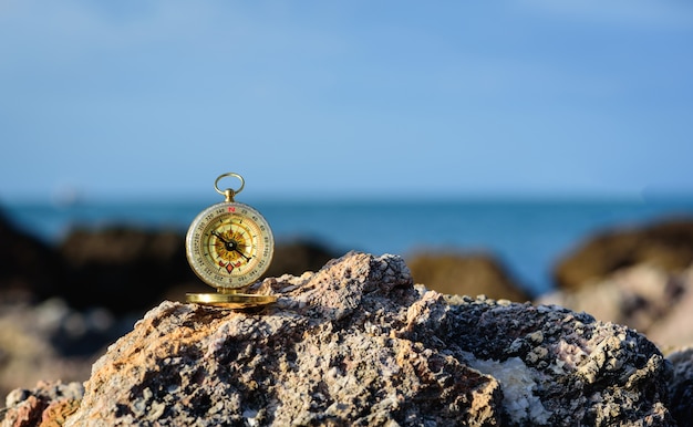 Analogical compass abandoned on the rocks with blurred sea background.
