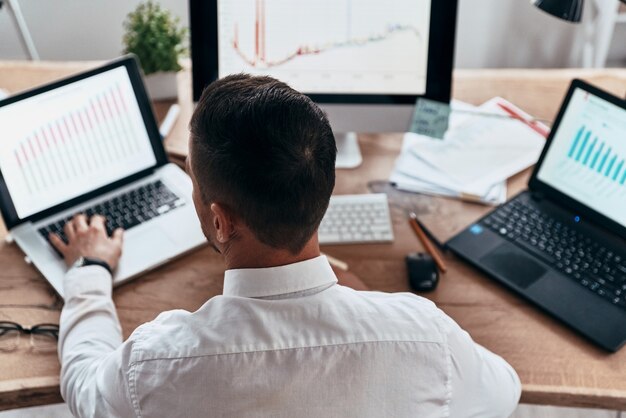 Analyseren van strategie. bovenaanzicht van een jonge zakenman in formalwear die gegevens analyseert met behulp van de computer terwijl hij op kantoor zit