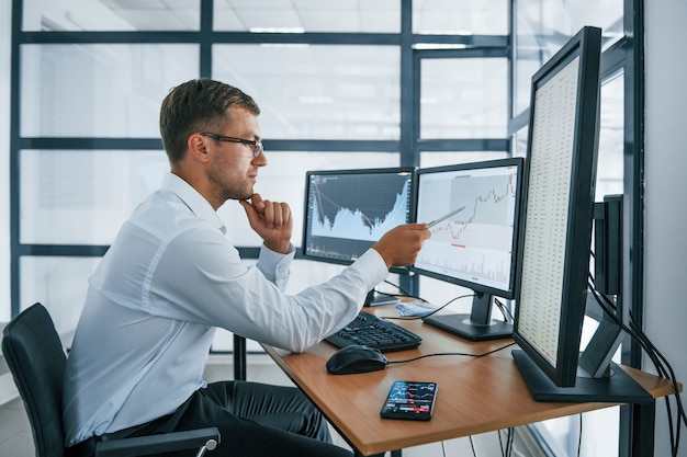 Analysing graphs. Young businessman in formal clothes is in office with multiple screens. Conception of exchange and money.