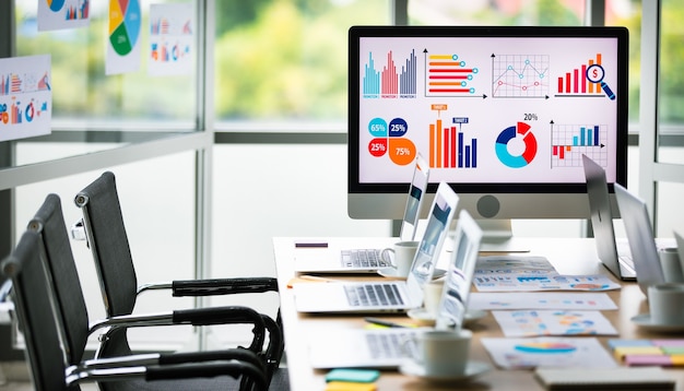 Analysis sales target growth graph chart investment report data on big computer screen monitor placed in middle of meeting table in front glass building windows with garden view in blurred background.