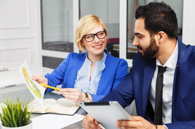 Processo di lavoro del team del manager analitico uomo barbuto e donna d'affari bionda vestita in giacca e cravatta lavorano con documenti infografici all'interno dell'ufficio bianco