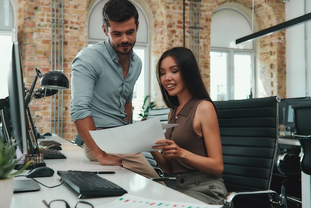 Analyzing results two cheerful young colleagues in casual wear examining documents while sitting