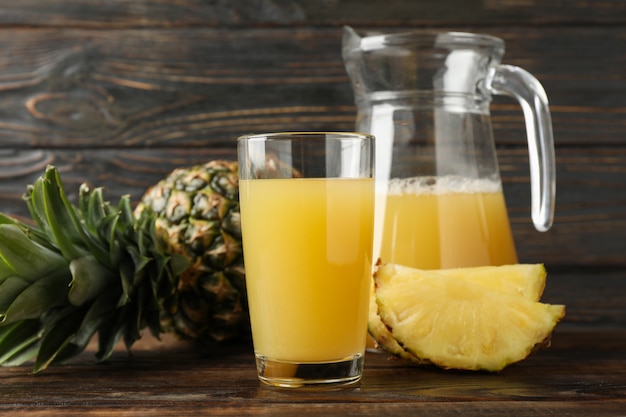 Ananas, glazen kan en glas met sap op hout, ruimte voor tekst