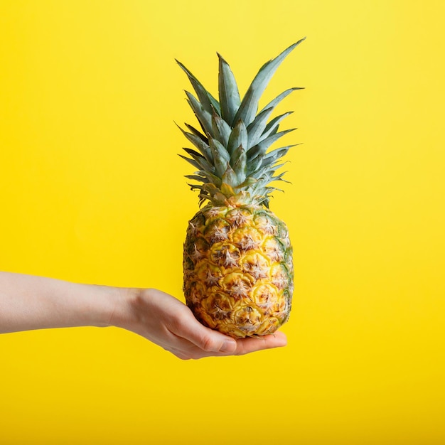 Foto ananas in de hand minimalistisch zomerconcept rijp sappig ananas tropisch fruit geïsoleerd op geel