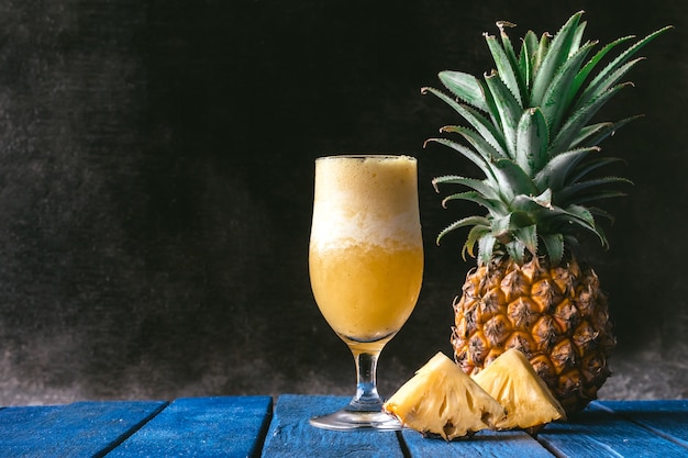 Ananas smoothie en vers ananasfruit op blauwe houten lijst met zwarte achtergrond.