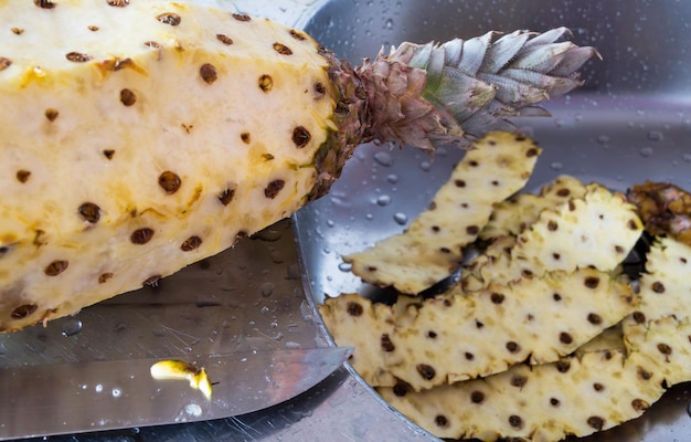 Ananas wordt geschild boven een roestvrijstalen gootsteen
