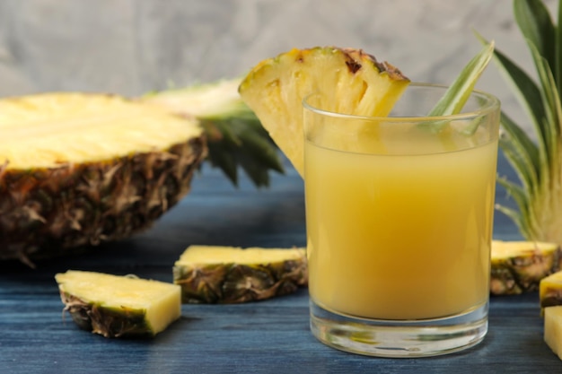 Ananassap in een glas en stukjes verse ananas op een blauwe houten achtergrond zomerfruit
