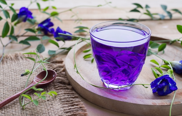 Photo anchan flower juice or blue pea flower herbal tea, butterfly pea in glass cup with wooden spoon on wooden table