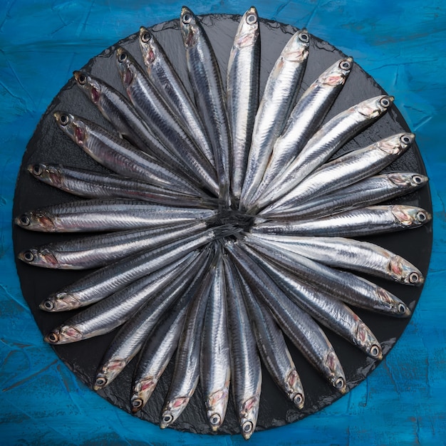 Anchovies in the shape of a circle on a black stone. Seafood. Small sea fish