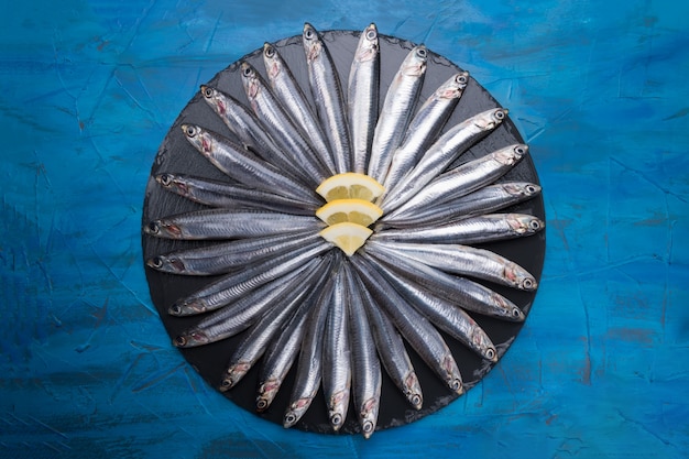 Anchovies in the shape of a circle on a black stone. Seafood. Small sea fish