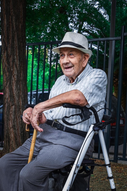 Photo anciano hombre mayor sentado en su andador con un baston sonriente con arrugas marcadas de la vejez