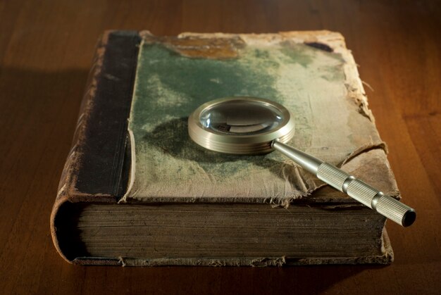 Photo an ancient book in a ragged cover and a magnifying glass on a table closeup