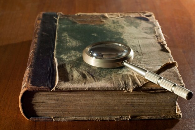 An ancient book in a ragged cover and a magnifying glass on a table closeup