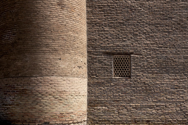 Ancient brick wall with window and round tower illuminated by side sunlight Bukhara Uzbekistan