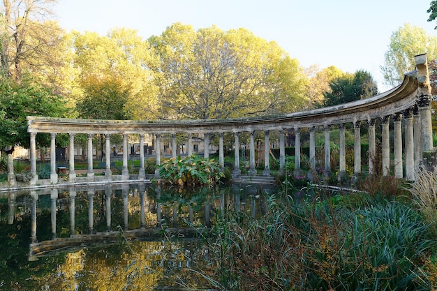 The ancient columns of Parc Monceau are reflected in the water of the oval basin in the sun This public garden is located in the 8th arrondissement of Paris