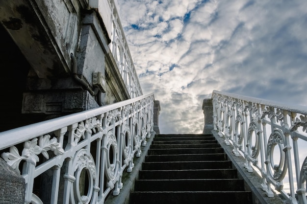 Ancient decorated staircase with beautiful handrails goes up towards a dramatic cloudy sky