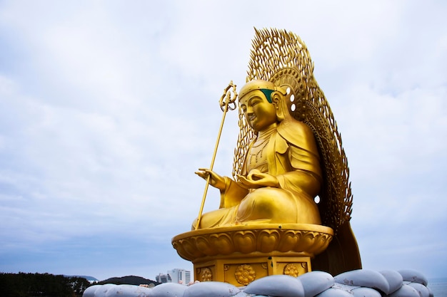 Ancient golden Jijang Bosal statue on stone rock cliffs for korean people travelers travel visit and respect praying blessing wish in Haedong Yonggungsa temple at Gijang in Busan or Pusan South Korea