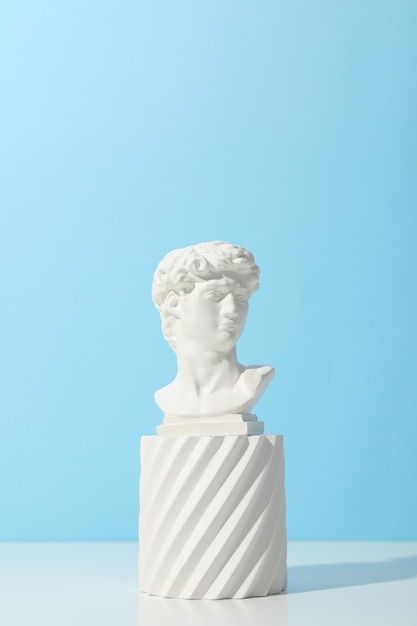 Ancient head on white table against blue background