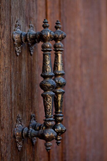 Ancient italian metal door handles on brown wooden door.