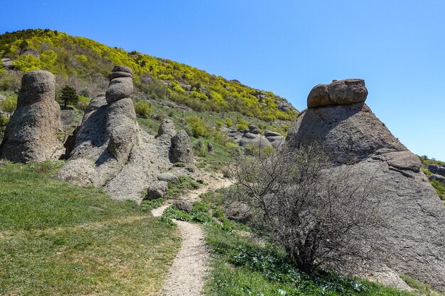 Ancient limestone high mountains of rounded shape in the air haze. The Valley of Ghosts. Demerji. Green trees and bushes in the foreground. May 2021. Crimea.