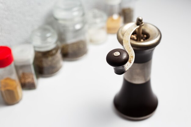 Ancient pepper mill near another seasonings on white surface.