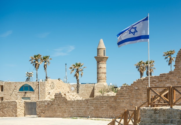 Ancient remnants of Ceasarea and waving flag of Israel in Maritima National Park in Caesarea Israel