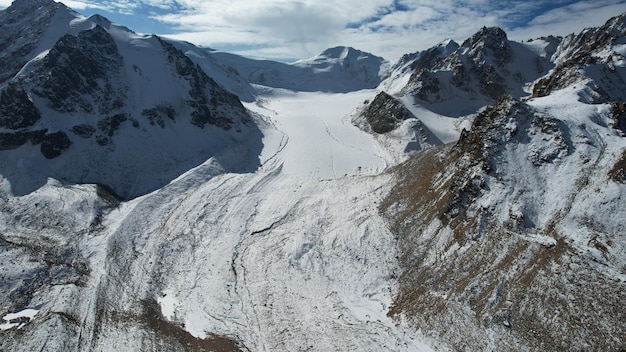 An ancient snow glacier among high mountains. In places there are steep cliffs and large rocks.