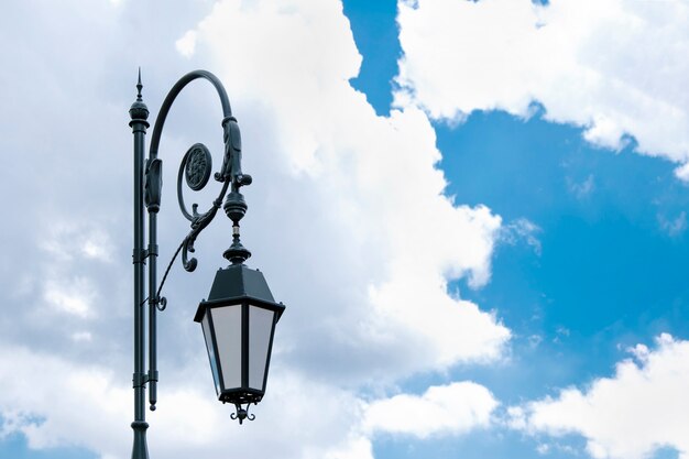 Ancient street lamp against a blue sky with clouds.