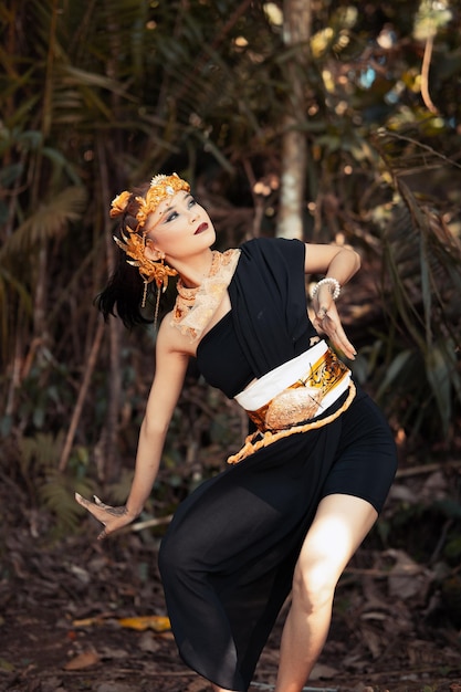 Ancient woman in her golden crown and golden necklace pose in her black dress inside the forest