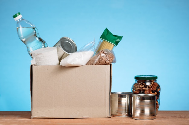 Ander eten in een vrijwilligersbox. doneer box, donatie en liefdadigheidsconcept. schenkingsdoos met voedsel op blauwe achtergrond.