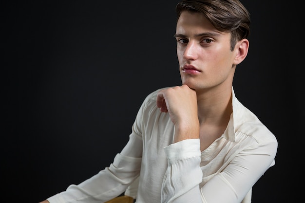 Androgyne man zittend op een stoel met hand op zijn kin