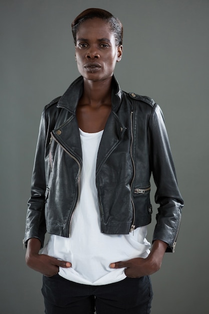 androgynous man in black jacket posing against grey wall