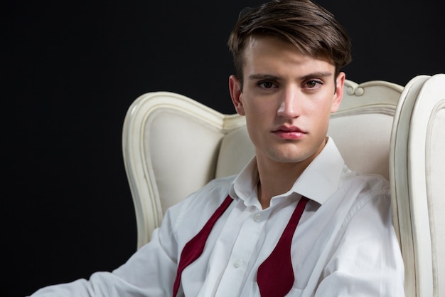 Androgynous man sitting on chair against black wall