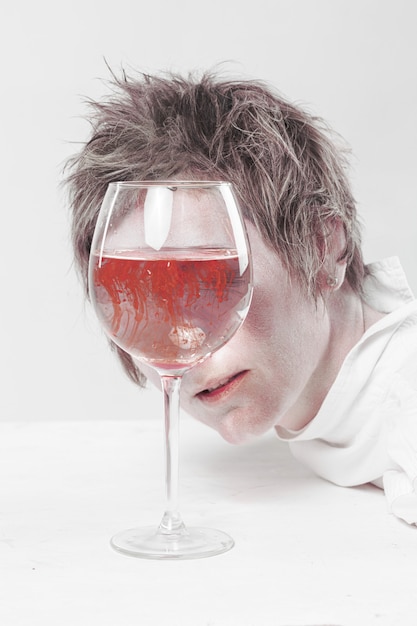 Androgynous woman with short haircut and white t-shirt looking into the glass full of spreading blood in the water.