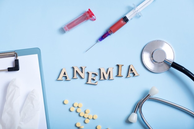 Anemia text with container for blood analysis stethoscope pills syringe flat lay top view