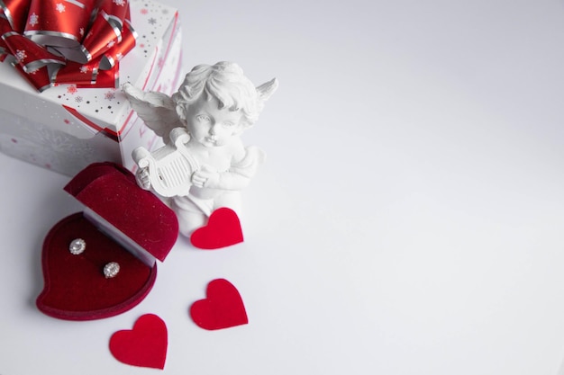 Angel,gift box and diamond earrings in red jewelery\
heart-shaped box on white background.