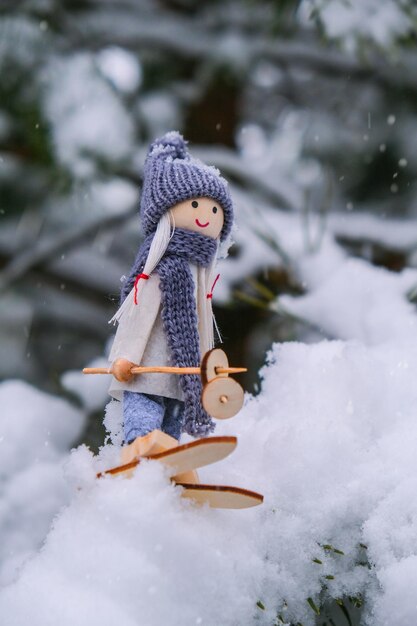 Foto gnomo angelo in sciarpa e cappello lavorato a maglia sciare su un ramo di abete innevato giocattolo elfo sugli sci in un paesaggio innevato