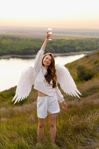 Photo angel holding glass of wine near the lake