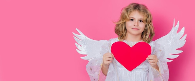 Angel kid with heart valentines day blonde cute child with angel wings on a pink studio background b