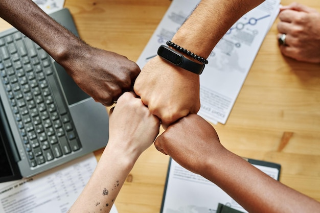 Photo above angle of four hands of young intercultural employees