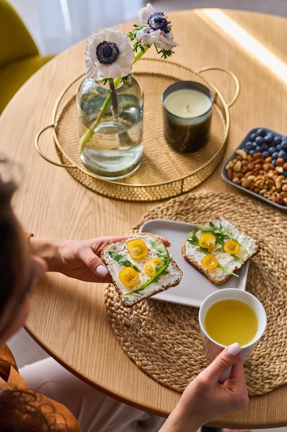 Above angle of girl holding sandwich and cup of orange juice over served table