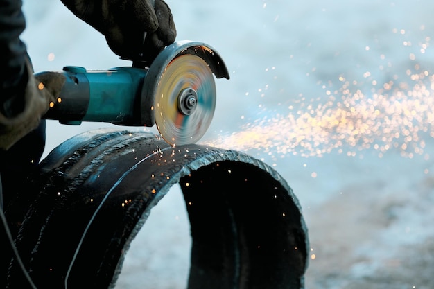 The angle grinder cuts a largediameter metal pipe and sparks fly Closeup of work in production