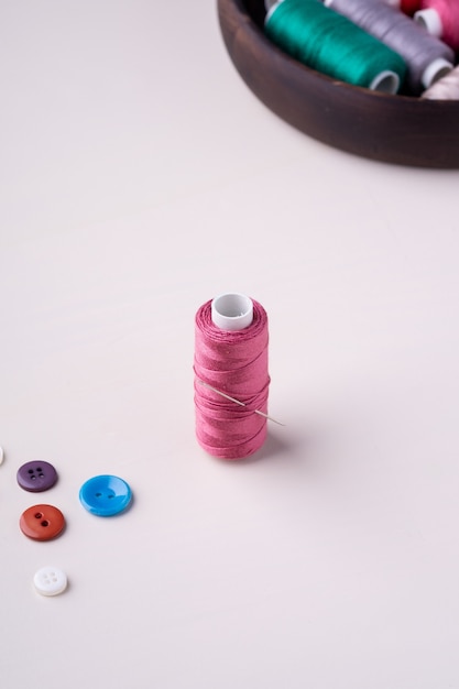 Photo angle view close up of pink thread coil with buttons and needle