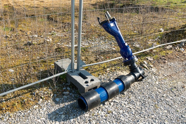 An angled plastic connecting pipe lying next to a metal fence