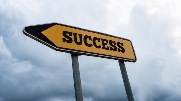 Angled signboard and arrow with the word - Success - pointing to the left against a cloudy sky in a conceptual image, low angle view.