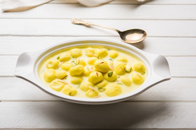 Photo angoori rasmalai is an indian dessert sweet with dry fruits and saffron toppings, served in a bowl over moody background. selective focus