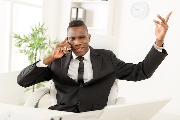 Angry African businessman in the office using mobile phone.