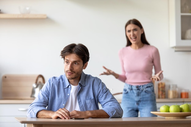 Photo angry aggressive millennial european wife yells at sad depressed husband at kitchen