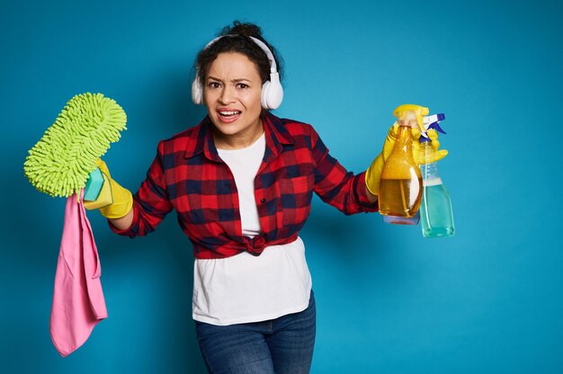 Angry american woman cleaning products in hands looking at the camera bewildered before upcoming homework